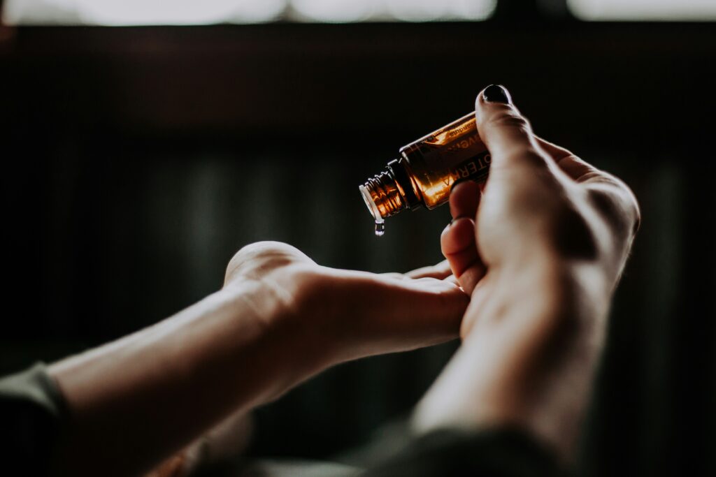 Essentiële haarolie druppelt uit een bruine glazen fles op een open handpalm, perfect voor het voeden en verzorgen van droog haar.